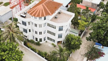 Un edificio de varios pisos con techo plano, rodeado de vegetación y un cielo despejado.