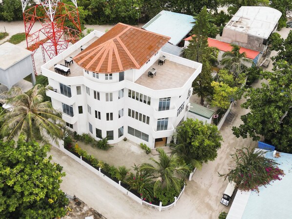 A multi-story building with a flat roof, surrounded by greenery and a clear sky. - Handhu Runbaa Inn (Dhangethi)