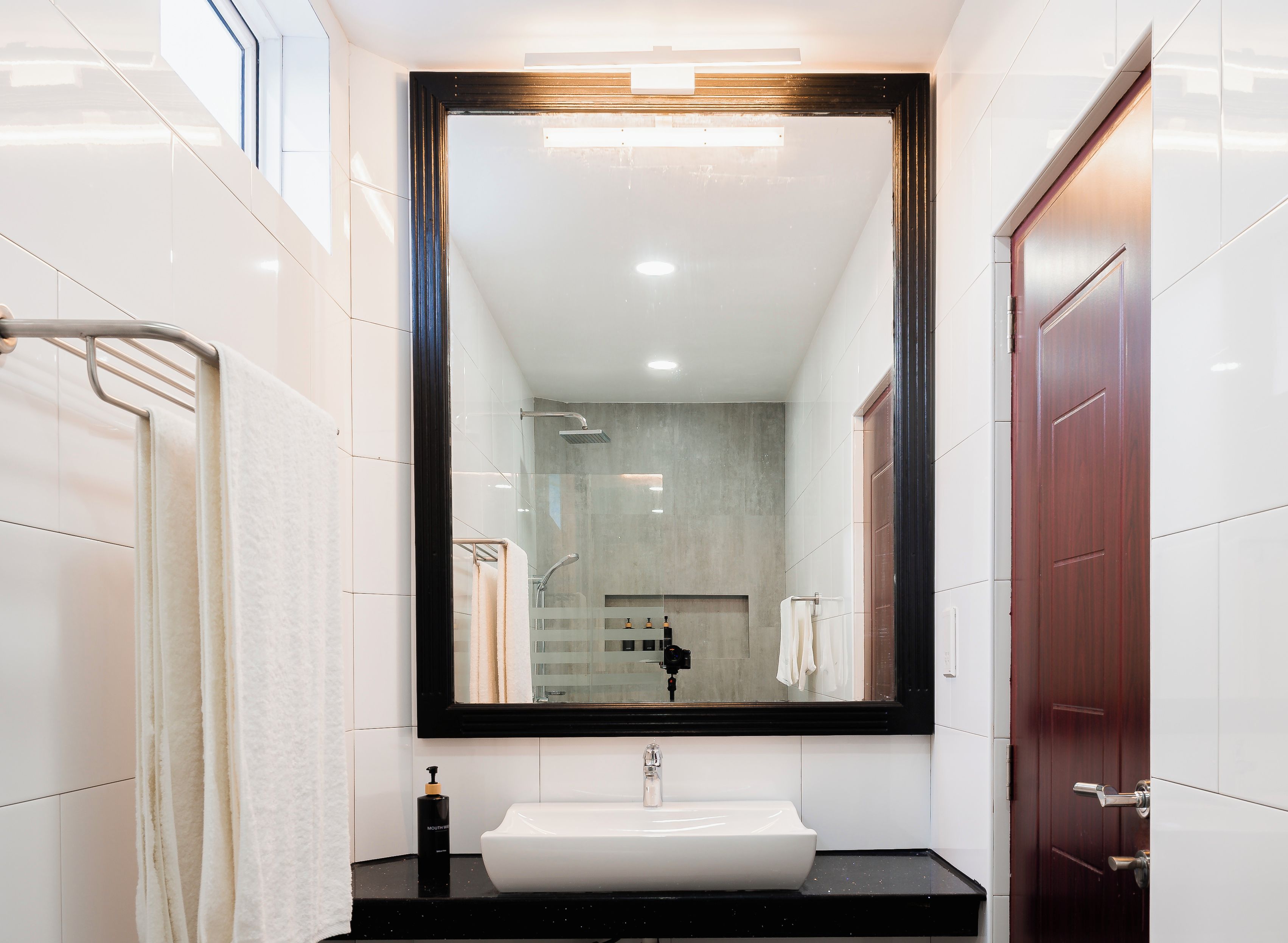Un baño moderno con un espejo grande, un lavamanos blanco y una zona de ducha.