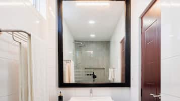 Un baño moderno con un espejo grande, un lavamanos blanco y una zona de ducha.