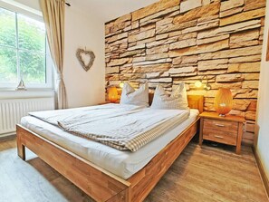 Ein Schlafzimmer mit Stewand, einem Bett mit Holzbettgestell, einem Nachttisch mit Lampe und einem Fenster mit Vorhängen.