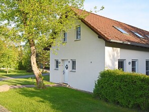 Ein zweistöckiges Haus mit geneigtem Dach, einer kleinen Veranda und einem gepflegten Rasen.