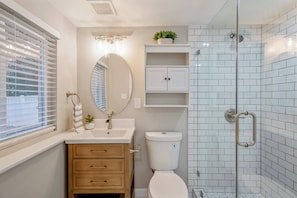 A bathroom with a toilet, sink, mirror, and shower. - 8 Bells Bungalow - Cozy, Stylish, Prime Location (Annapolis)