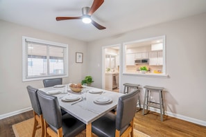 A dining area with a table set for four, a ceiling fan, and a view into the kitchen. - 8 Bells Bungalow - Cozy, Stylish, Prime Location (Annapolis)