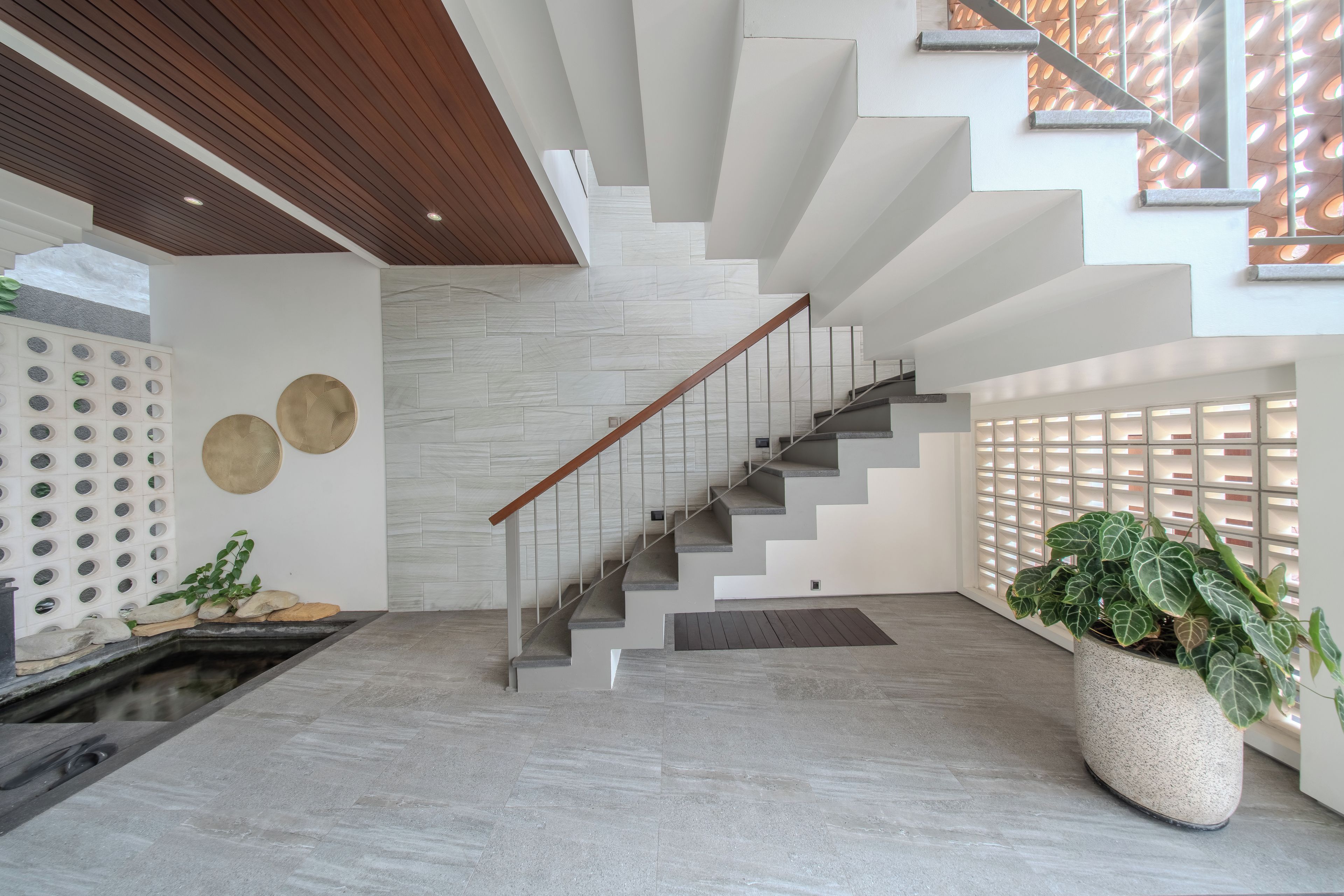 Un interior moderno con una escalera, una pared con espejos circulares y una gran planta en maceta.