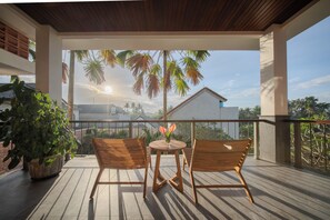 A balcony with two wooden chairs and a small table, overlooking a residential area with palm trees and a clear sky. - Andara Hide Ubud villa (Gianyar)