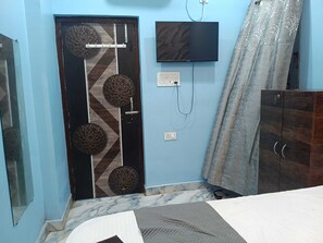 A room with a door featuring decorative circular patterns, a flat-screen TV mounted on the wall, and a wardrobe with two doors. - Hotel Atithi (Patna)