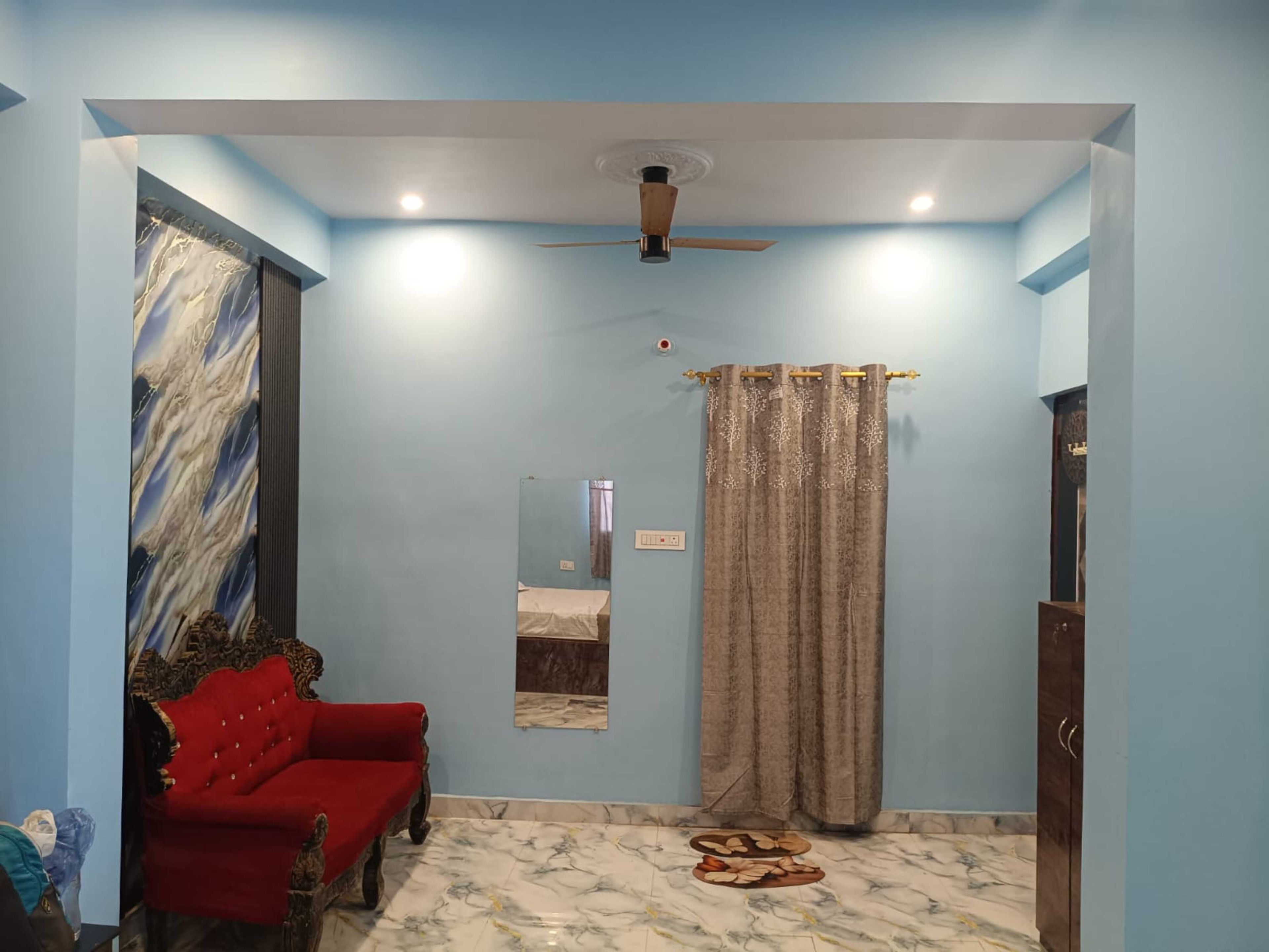 Una habitación con ventilador de techo, un sofá rojo, un espejo y una cortina.