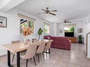 Una sala moderna con sofá, una mesa de comedor con sillas, un ventilador de techo y un televisor.