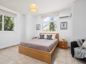 Un dormitorio con cama, mesita de noche, silla y ventana.