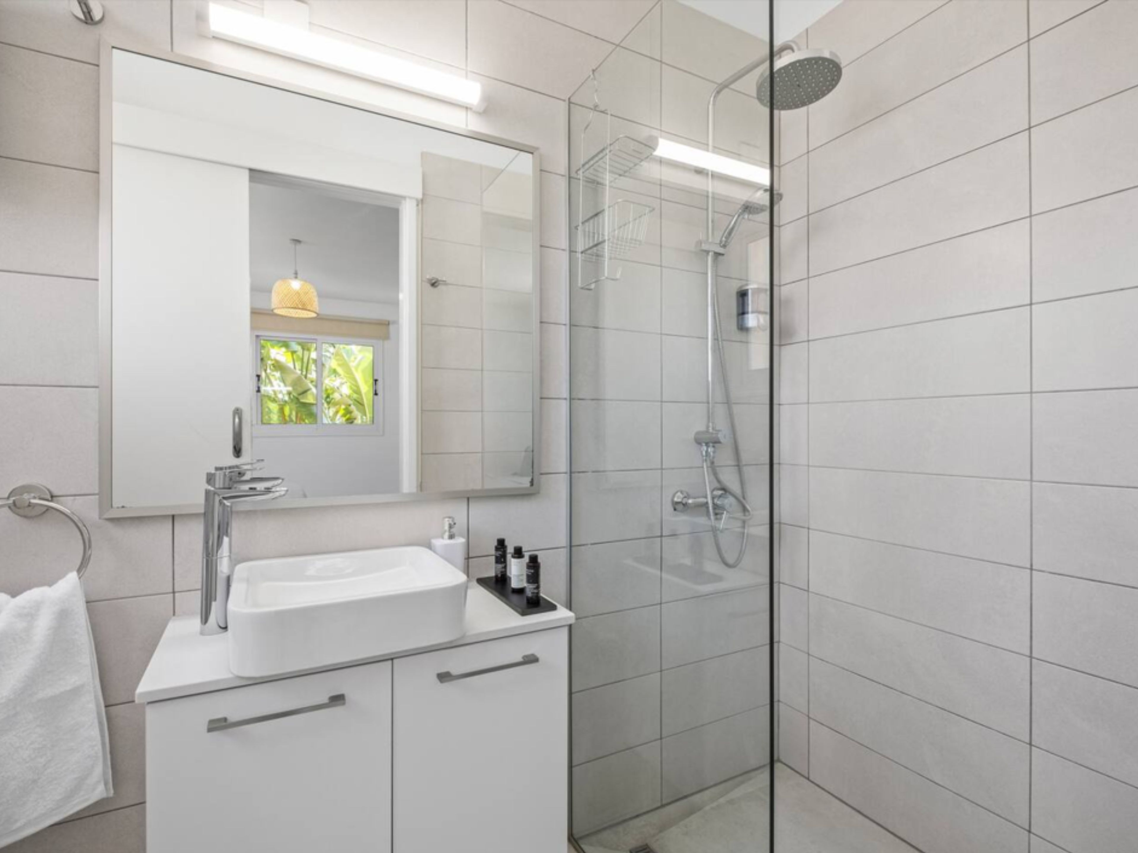 Un baño moderno con ducha envuelta en vidrio, un lavabo blanco y un espejo sobre él.
