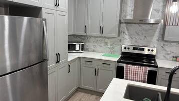 A modern kitchen with stainless steel appliances, white cabinetry, and a marble backsplash.