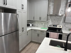 Cozinha moderna com eletrodomésticos de aço inoxidável, armários brancos e painel de fundo de mármore.