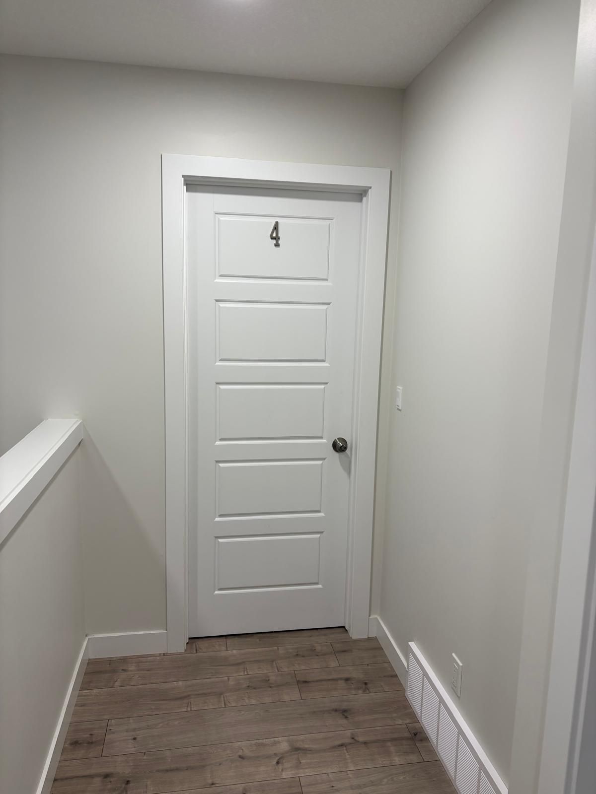 Una puerta blanca con el número 4, piso de madera y zócalo blanco.