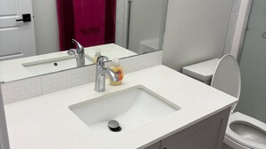 Ein Badezimmer mit einem weißen Waschbecken, einem Spiegel, einer Dusche und einer Toilette.
