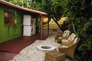A covered outdoor area with a washing machine, wicker furniture, and a concrete fire pit. - Iconic Wynwood Artsy Bungalow - Walk to Everywhere (Miami)