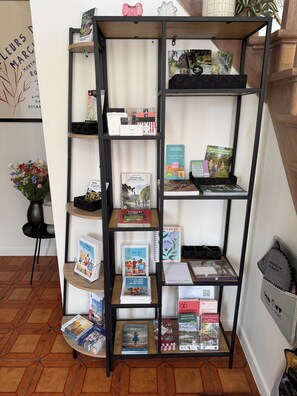 A bookshelf with various books and magazines, a small table with a vase of flowers, and a framed picture on the wall.
