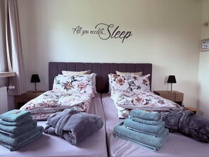 A double bed with floral bedding, two bedside tables with lamps, and a wall with a motivational quote.