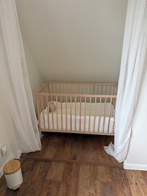A crib with a wooden frame and white bedding, positioned against a wall with white curtains. - Maison François: a vacation home for a carefree stay surrounded by nature near Bruges (Oostkamp)