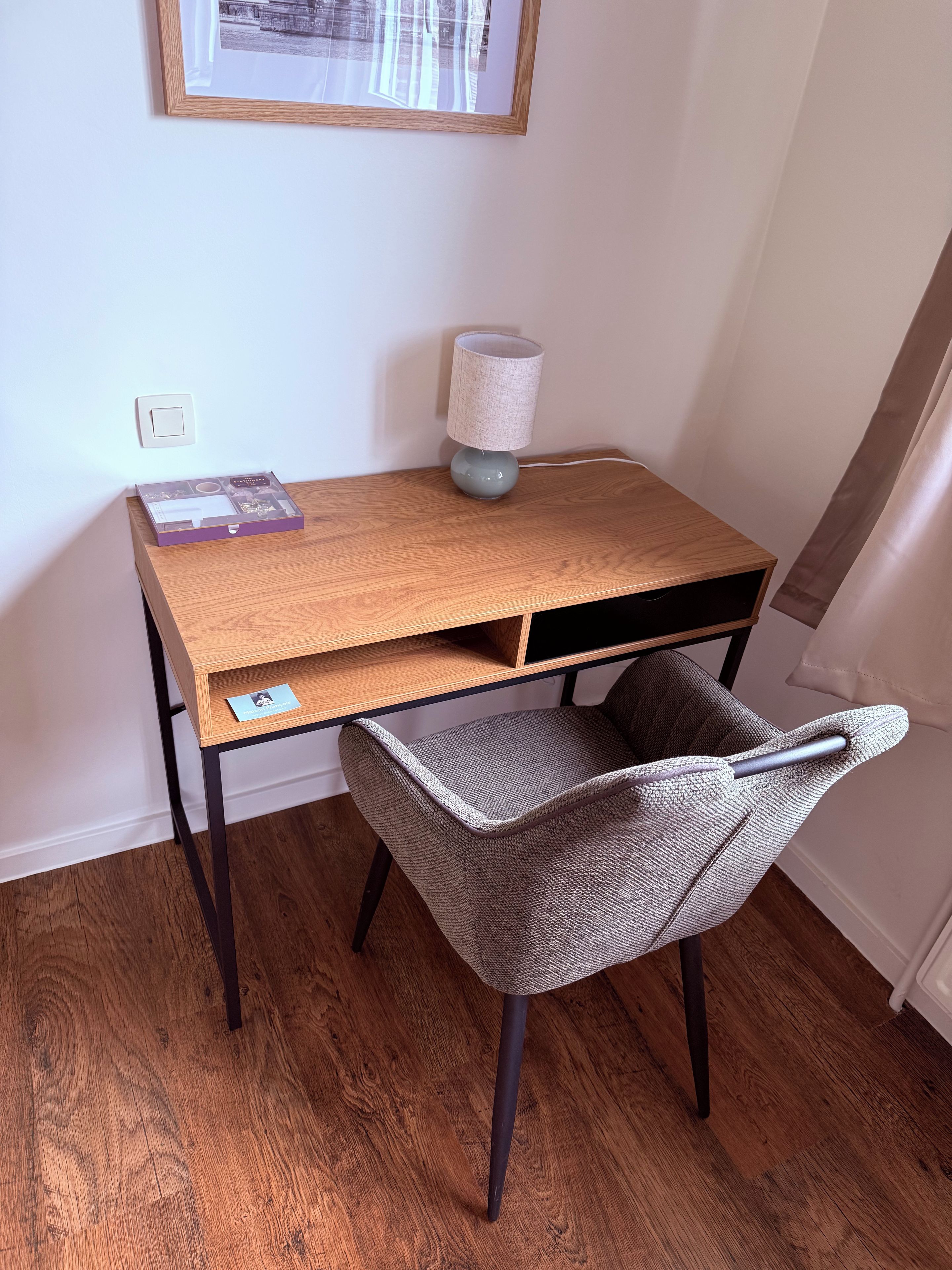 Un bureau en bois, une lampe, une chaise et un tableau encadré accroché au mur.