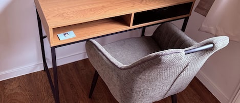 Un bureau en bois, une lampe, une chaise et un tableau encadré accroché au mur.