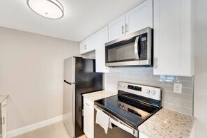 A modern kitchen with stainless steel appliances, white cabinetry, and a tiled backsplash. - Port Charlotte Pool Retreat (Port Charlotte)