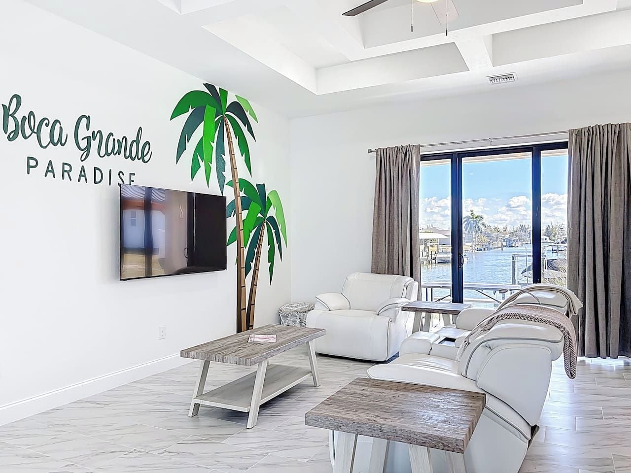 Una sala de estar moderna con un televisor de pantalla plana grande, sofás de cuero blanco, una mesa de centro de madera y una planta grande en maceta.