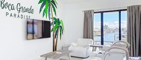 Una sala de estar moderna con un televisor de pantalla plana grande, sofás de cuero blanco, una mesa de centro de madera y una planta grande en maceta.