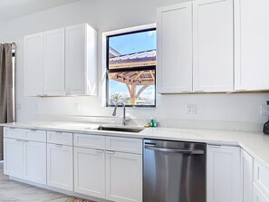 A modern kitchen with white cabinetry, a stainless steel dishwasher, and a window with a view of a building's roof. - Boca Grande Retreat 4BR 2BA Waterfront Sleeps 12 (Port Charlotte)