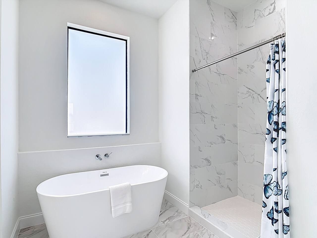 A modern bathroom with a freestanding bathtub, a shower with a marble wall, and a curtain with a butterfly pattern.
