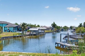 A waterfront property with a dock, a covered area, and a house with a blue exterior. - Boca Grande Retreat Sleeps 10 (Port Charlotte)