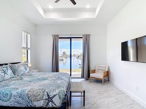 Ein Schlafzimmer mit Bett, einem Sessel, einem Fernseher und Blick auf einen Pool.