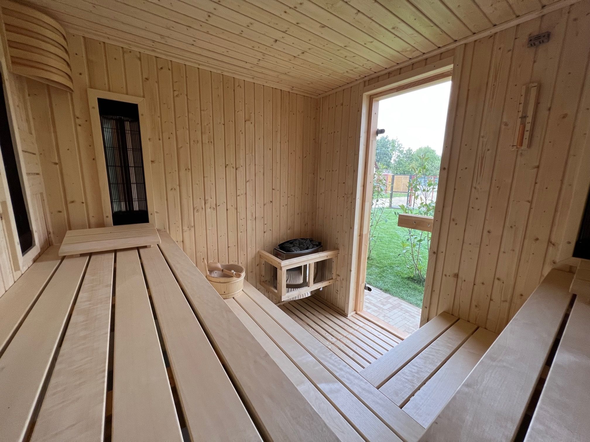 Une cabine de sauna en bois avec des bancs, un banc sur lequel se trouve un objet noir, et une petite structure en bois sur laquelle repose un objet noir.