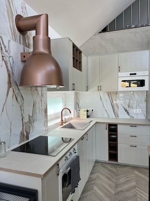 A modern kitchen with marble backsplash, stainless steel appliances, and a copper pendant light.