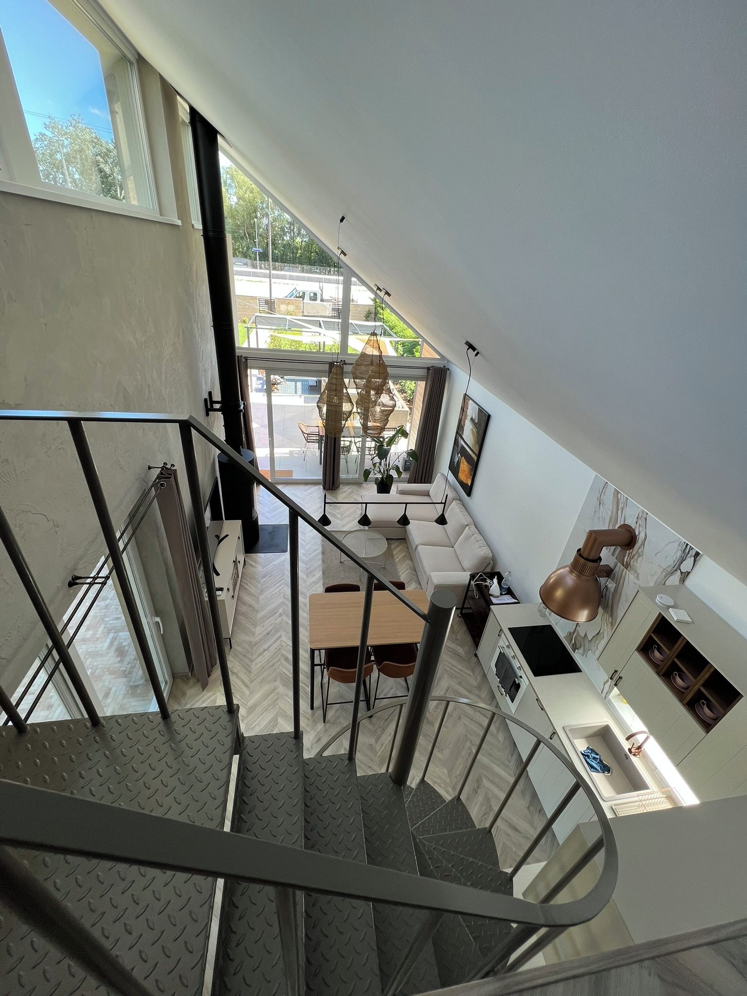 A modern interior with a staircase leading to a dining area, kitchen, and a view of the outdoors.