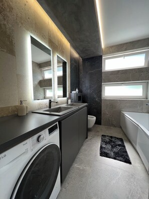A modern bathroom with a washing machine, a sink, and a toilet.