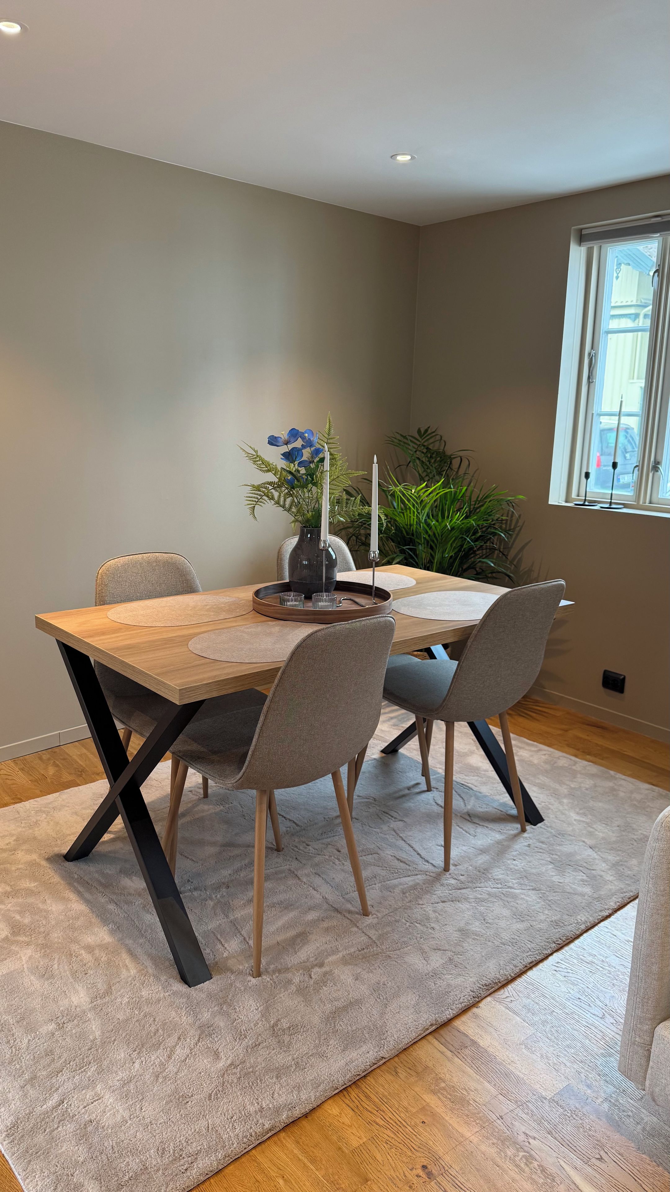 En matplats med ett träbord, fyra stolar, en vas med blommor och ett fönster med utsikt.
