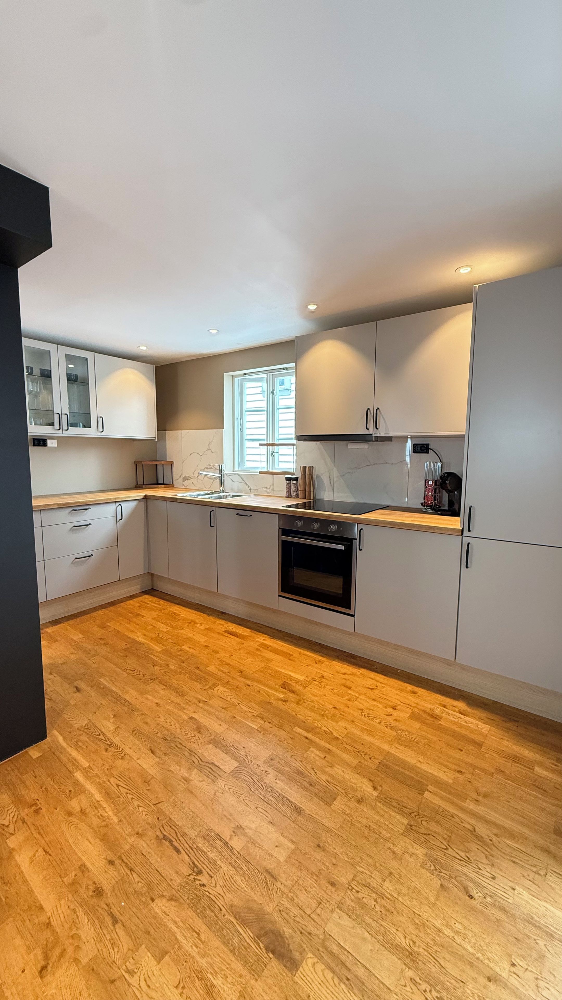 A modern kitchen with a wooden countertop, built-in cabinets, and a window.