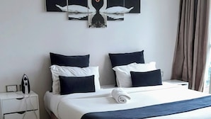 Quarto de hotel moderno com uma cama grande, uma mesinha de cabeceira com um ferro de passar e uma obra de arte na parede retratando cisnes.
