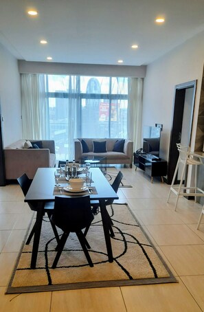A modern living room with a dining area, large windows, and a view of the city. - Luxury 2 Bedroom Apartment With Pool in Westlands, Skynest (Nairobi)