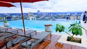 Área de piscina no terraço com espreguiçadeiras, um guarda-sol vermelho e plantas em vasos.