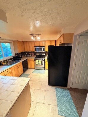 A kitchen with wooden cabinets, a black refrigerator, a microwave, and a stove. - Gorgeous 3-bedroom house with AC in charming Eugene (Eugene)
