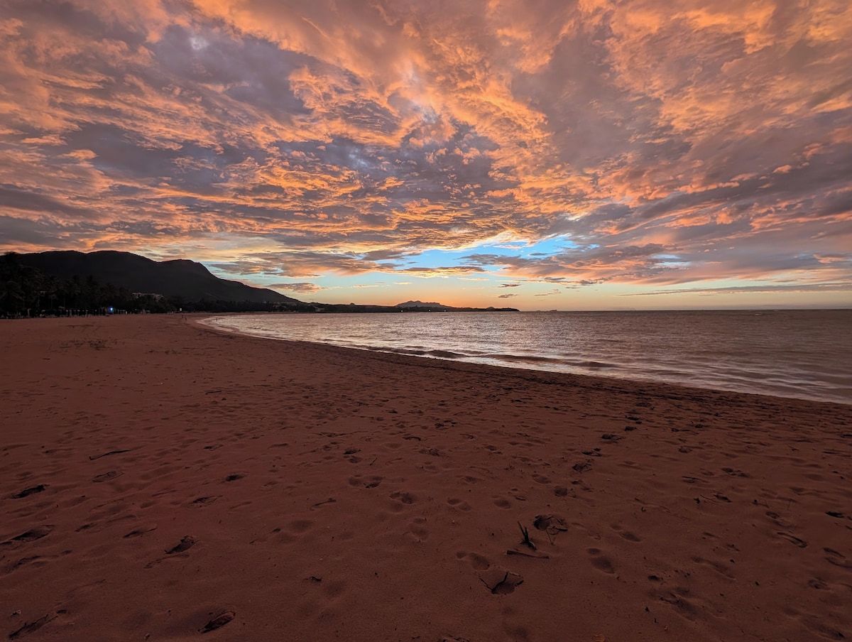 A beach with footprints leading to the water, a clear sky, and distant mountains.