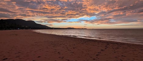 A beach with footprints leading to the water, a clear sky, and distant mountains.