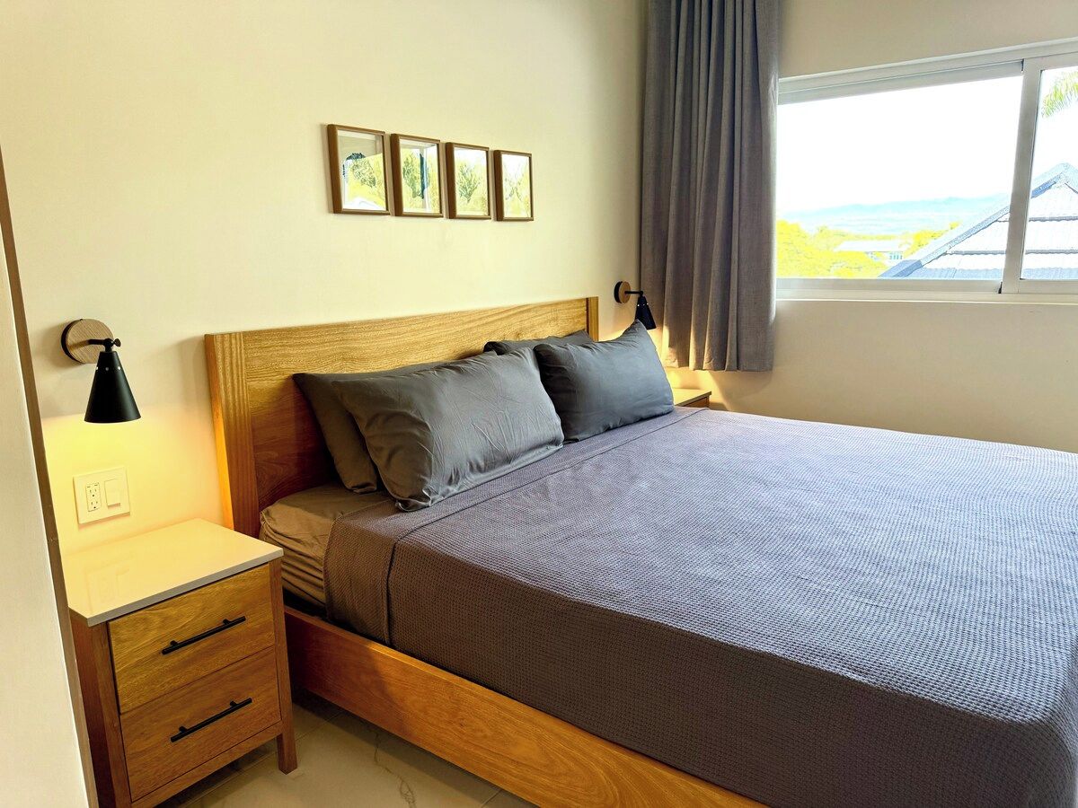 Une chambre à coucher avec un lit en bois, une table de chevet avec une lampe, une commode et une fenêtre avec des rideaux.