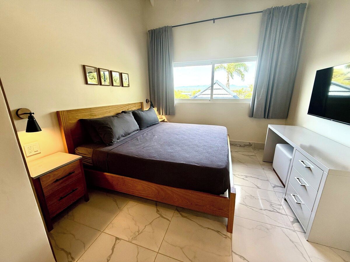 Un dormitorio con cama, mesita de noche, lámpara y televisor.