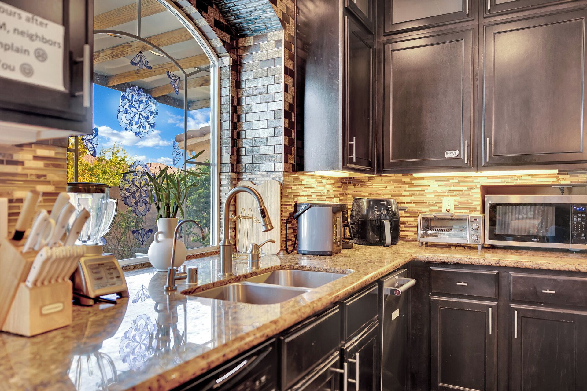 A modern kitchen with dark cabinetry, a granite countertop, a built-in microwave, and a coffee maker.