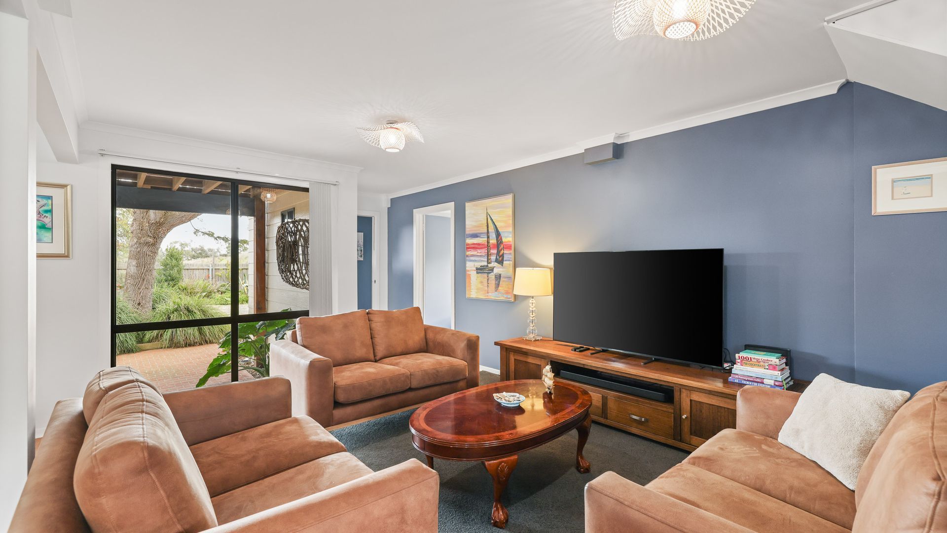 A living room with a large TV, two sofas, a coffee table, and a view of greenery outside.