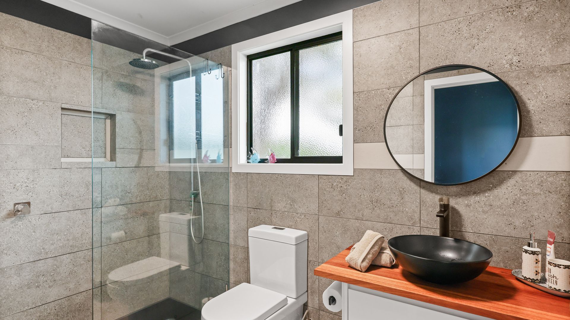 Een moderne badkamer met een douchecabine van glas, een toilet, een wastafel met een ruime wasbak en een spiegel.