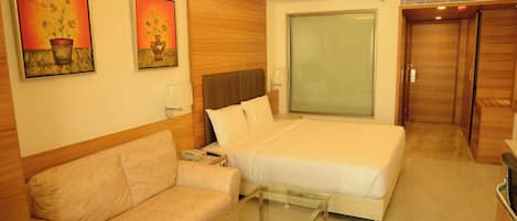 A hotel room with a bed, a sofa, a glass coffee table, and two paintings on the wall.
